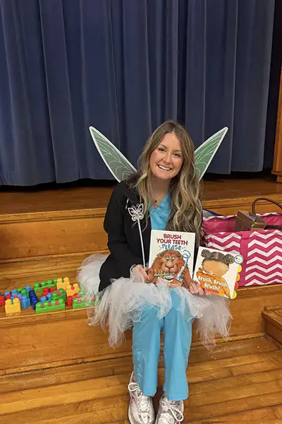 Salisbury Pediatric Dentistry's staff in a tooth fairy dress and books smiling at NC Pediatric Dentistry 