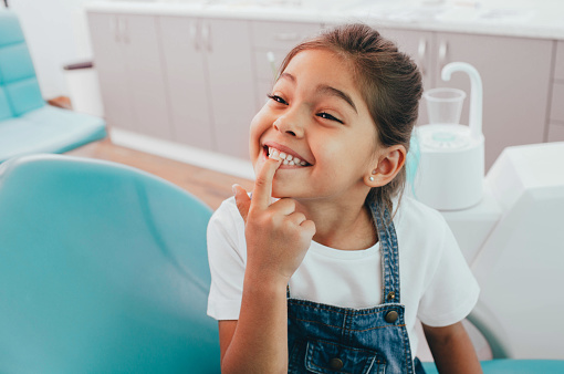 Adorable little girl pointing at her bottom teeth as she smiles