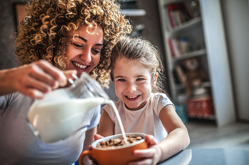 Mom puring daughter milk into her bowl of cereall
