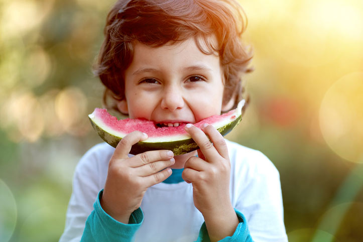 Little boy eating a large piece of watermelon.