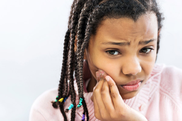 Young girl holding her cheek due to a tooth ache. Young girl holding her cheek due to a tooth ache.