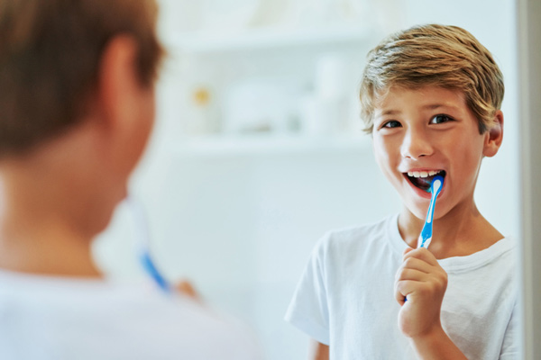 Young boy looking at a mirror and brushing his teeth.