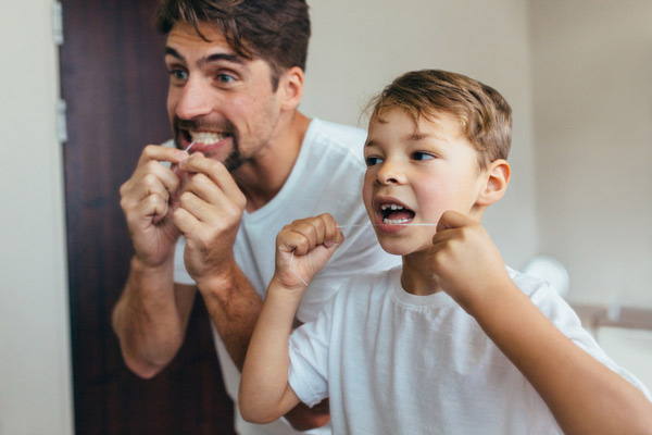 Young boy and parent flossing their teeth next to each other in the bathroom.