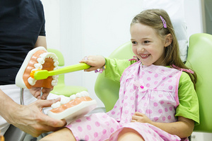 Little girl brushing large fake teeth at the dentist