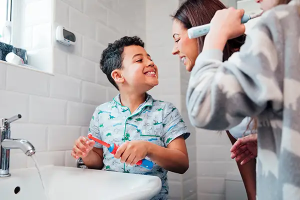 Mother and young son smiling while brushing their teeth together in a bright bathroom, demonstrating a family dental hygiene routine.
