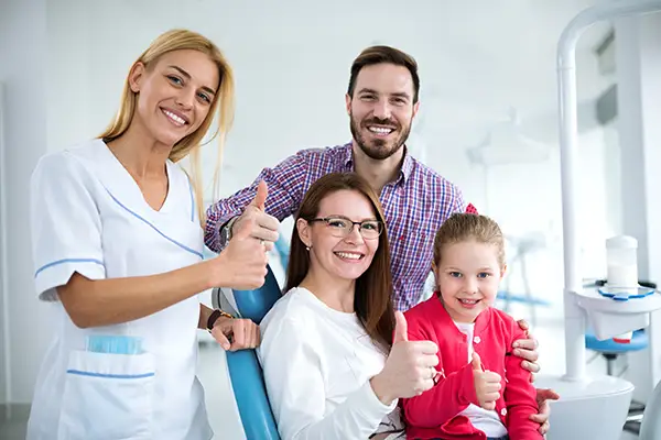 A satisfied family giving a thumbs up with the hygienist at the dentist office, suggesting a successful dental visit. A satisfied family giving a thumbs up with the hygienist at the dentist office, suggesting a successful dental visit.
