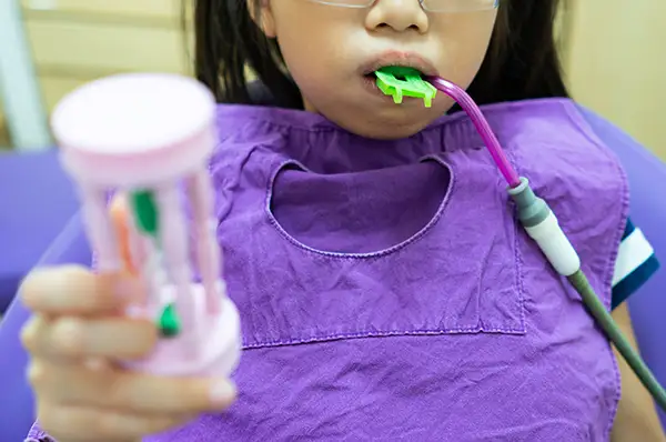 A young girl wearing a purple bib in the dentist chair while receiving a fluoride treatment.