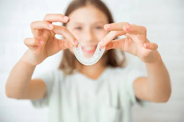 Young girl showing off her a clear mouth guard with a cheerful expression, promoting dental protection for kids.