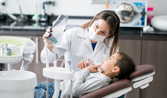 Young patient in dental chair while dentist holds a handheld mirror for him