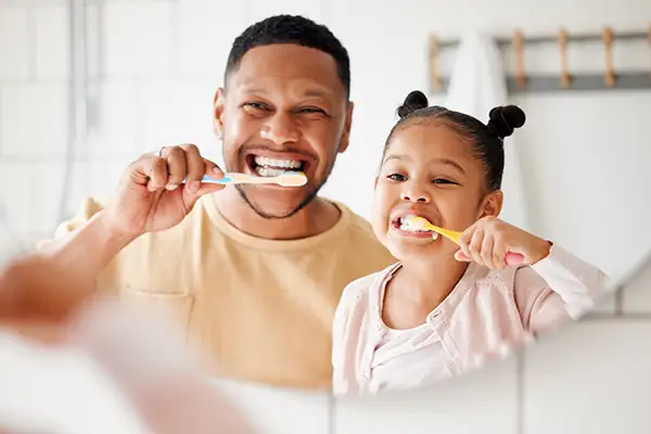Father and daughter brushing their teeth together, promoting good oral hygiene habits as part of preventive dentistry.